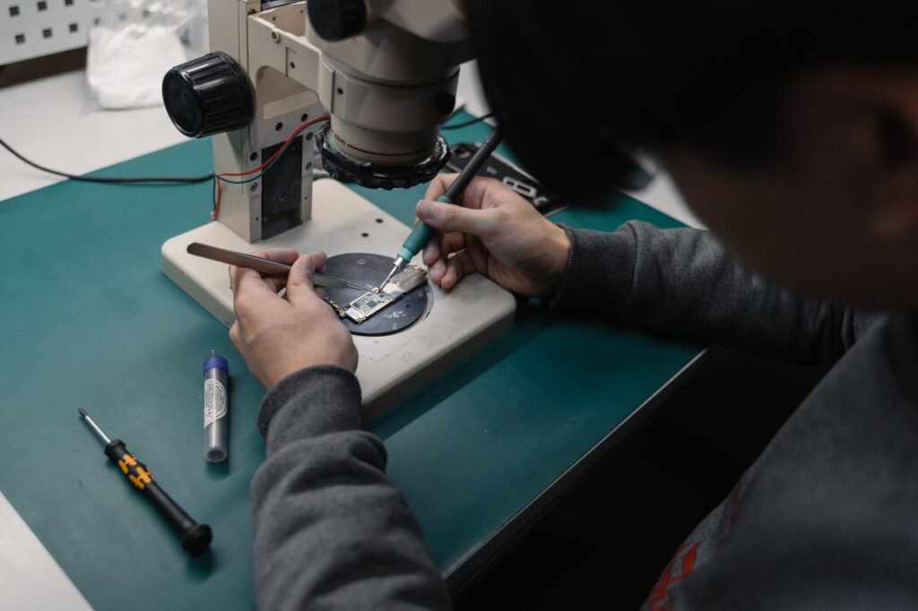 pexels-photo-6755066-6755066 Technician using a microscope to repair a broken electronic board with precision tools.