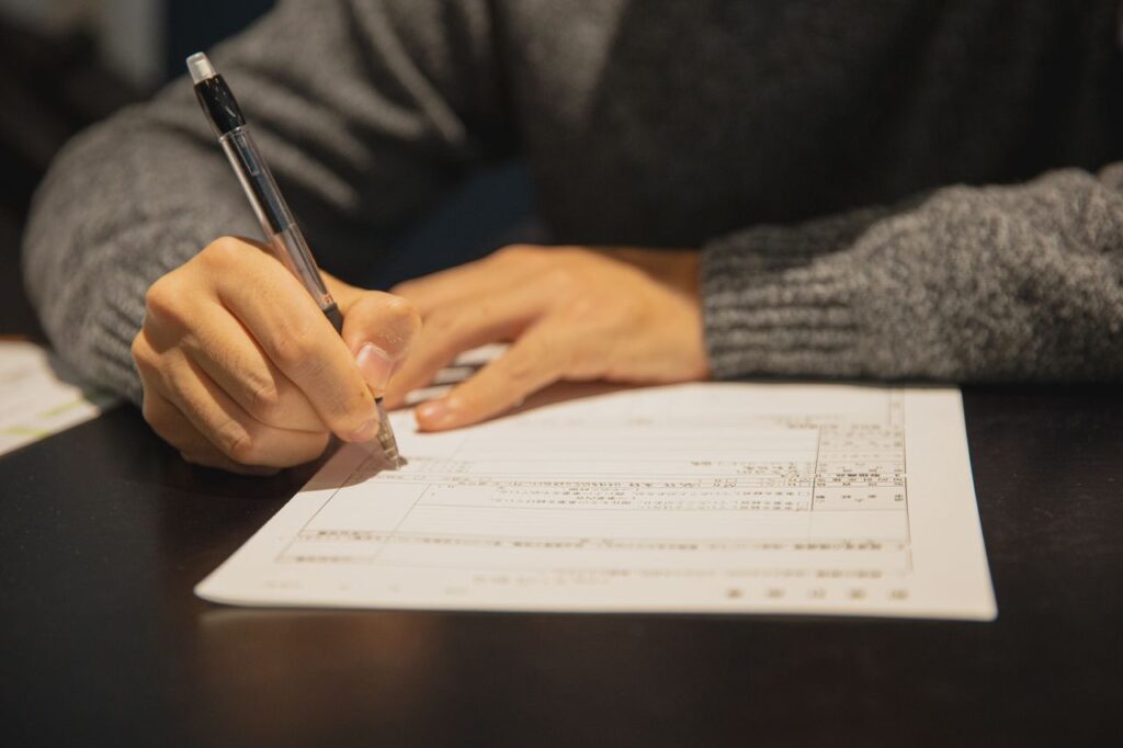 pexels-photo-6249395-6249395 Crop anonymous male in gray sweater writing in form of important document at table