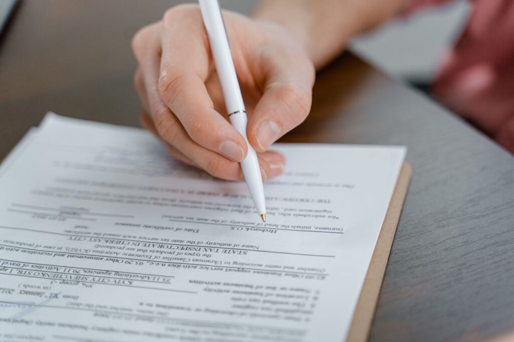 pexels-photo-7567551-7567551 A hand holding a pen signing a document, close-up shot with focus on the paper.