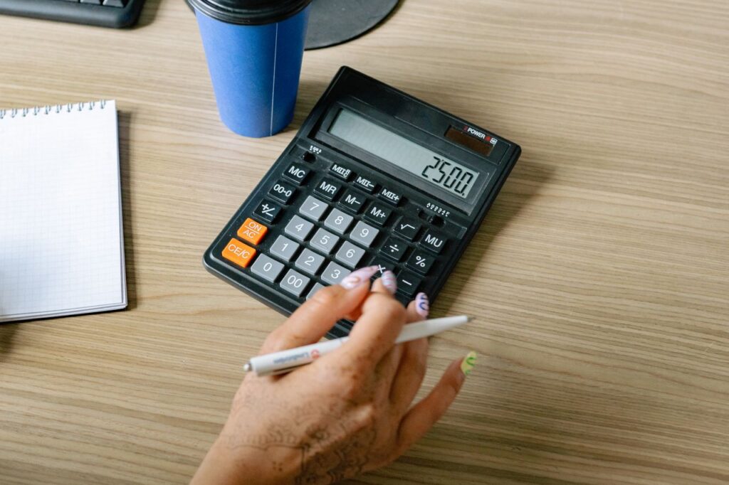 pexels-photo-8837378-8837378 A person uses a calculator and pen on a wooden surface, focusing on office work.